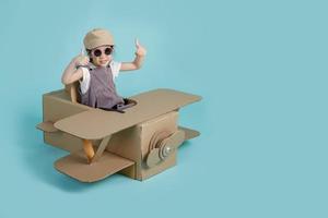 Asian little child girl playing with cardboard toy airplane handicraft isolated on blue long banner with copy space for your text, Creative at home and dreams of flight concept photo