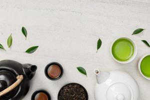 Cup of hot tea with teapot, green tea leaves and dried herbs top view on the white stone table empty space, Organic product from the nature for healthy with traditional style photo