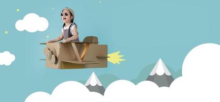 Asian little child girl playing with cardboard toy airplane handicraft over the clouds on blue sky long banner with copy space for your text, Creative with family and dreaming of flying concept photo