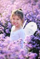 linda niña sonriente usa un traje de hada de ballet mágico en el hermoso campo de flores púrpura de margaret. foto