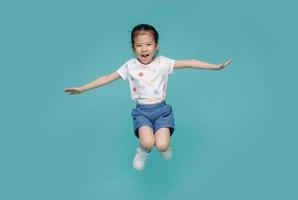 Una niñita asiática emocionada saltando en el aire, espacio vacío en una foto de estudio aislada en un fondo azul colorido