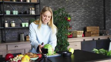 mujer joven en una cocina con ingredientes frescos y dispositivo de teléfono inteligente video
