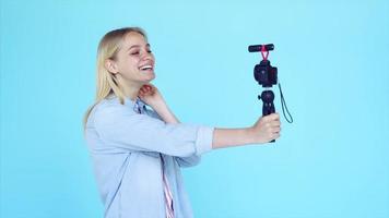 Vlogger uses camera and selfie stick to record video blog in front of a blue background