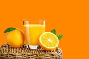 Glass of fresh orange juice on a basket, Fresh fruits Orange juice in glass with group on orange color background with copy Space for your text. photo