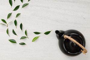Teapot with organic green tea leaves on the white stone desk empty space creative flat lay, Organic product from the nature for healthy with traditional style photo