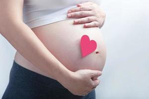 Pregnant woman with single pink heart on her baby bump. All on white background. photo