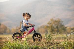 Happy child riding a bike. Little girl on a pink bicycle. Healthy preschool children summer activity. Kids playing outside. Little girl learns photo