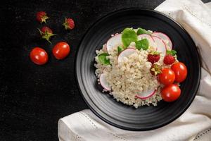 Quinoa salad with vegetables, raspberry and tomatoes on the black table. Super food for healthy and concept of balanced diet photo
