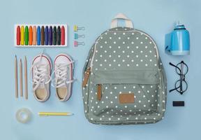 flatlay creativo de educación mesa azul con mochila, zapatos, lápices de colores, anteojos, aislado sobre fondo azul, concepto de educación y regreso a la escuela foto