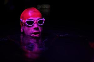 nadador triatleta auténtico que tiene un descanso durante el entrenamiento duro en la luz de gel de neón nocturno foto