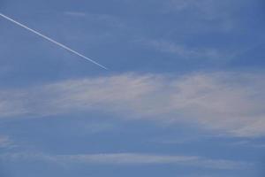 un avión volando en el cielo azul y las nubes. una estela blanca de un avión en el cielo de verano. foto