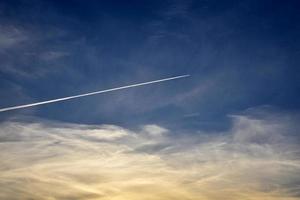 un avión volando en el cielo azul y las nubes. una estela blanca de un avión en el cielo de verano. foto