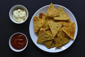 deliciosos nachos picantes en un plato con salsas sobre un fondo negro. delicioso bocadillo con primeros planos de nachos de maíz. foto