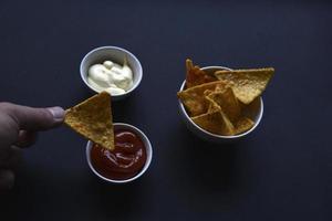 Delicious peppery nachos on a plate with sauces on a black background. Delicious snack with corn nachos close-up. photo