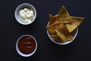 deliciosos nachos picantes en un plato con salsas sobre un fondo negro. delicioso bocadillo con primeros planos de nachos de maíz. foto