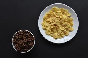 desayuno de copos de maíz de chocolate y miel en platos blancos sobre un fondo negro. delicioso desayuno de primeros planos de copos de maíz. foto