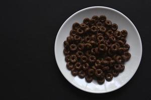 Breakfast of chocolate and honey cornflakes on white plates on a black background. Delicious breakfast of cornflakes close-up. photo