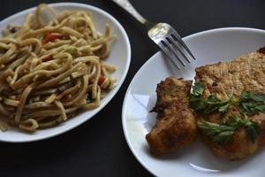 Delicious breakfast with noodles and a piece of fried pork on a white plate on a black background. A delicious breakfast is served with a hand and fork. photo