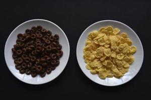 Breakfast of chocolate and honey cornflakes on white plates on a black background. Delicious breakfast of cornflakes close-up. photo