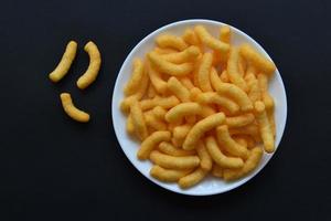 Corn salted and peppered chips on a white plate. Delicious breakfast of corn chips on a black background. photo