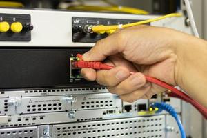 mano de un hombre que sostiene los cables de red para conectar el puerto de un conmutador para conectar la red de Internet, tecnología de comunicación conceptual foto