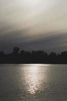 Atmospheric sunset behind trees and reflection in water. photo