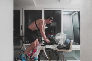 Man cycling on the machine trainer he is exercising in the home at night playing online bike racing game photo