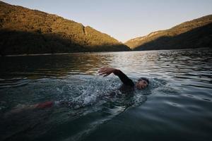 triathlon athlete swimming on lake in sunrise  wearing wetsuit photo