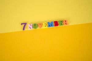 November 7 on a yellow, paper background with multicolored and wooden letters with space for text. photo