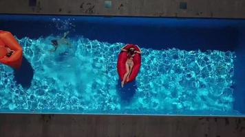 Aerial view of a pool with women on bright red and orange floats video