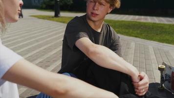 Teenage boy and girl hanging out at the park with a skateboard video