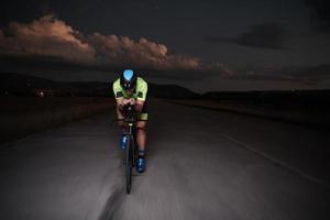 atleta de triatlón montando bicicleta rápido por la noche foto