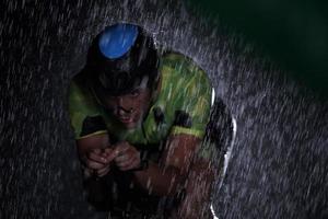 triathlon athlete riding bike  fast on rainy night