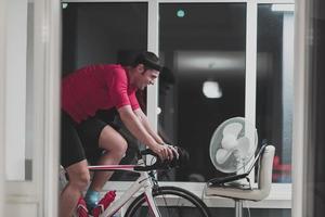 Man cycling on the machine trainer he is exercising in the home at night playing online bike racing game photo