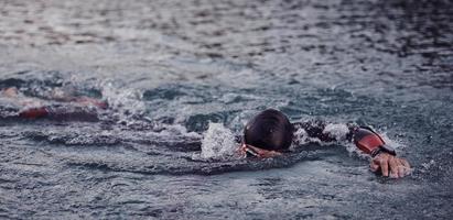 atleta de triatlón nadando en el lago al amanecer usando traje de neopreno foto