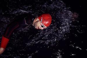 atleta de triatlón nadando en la noche oscura con traje de neopreno foto