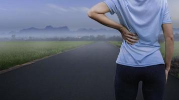 Asian fitness woman running and jogging outdoors on a country road in the morning and has back pain. photo