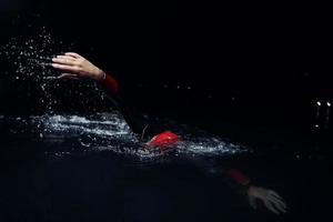 atleta de triatlón nadando en la noche oscura con traje de neopreno foto
