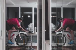 Man cycling on the machine trainer he is exercising in the home at night playing online bike racing game photo