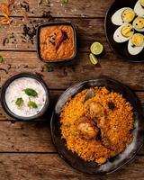 pollo biryani un plato indio que viene en un conjunto de alimentos a base de arroz hecho con especias, arroz y pollo y servido con salsa de berenjena y cebolla raitha como acompañamiento. foto