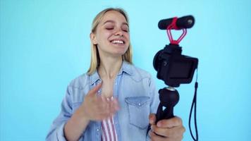 Vlogger uses camera and selfie stick to record video blog in front of a blue background