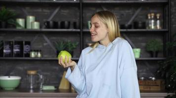 junge blonde Frau in der Küche isst einen grünen Apfel
