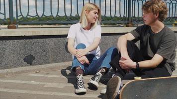 Teenage boy and girl hanging out at the park with a skateboard video