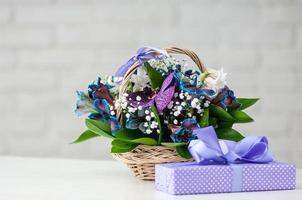 A present next to a composition with orchids, blue alstroemeria, lilies, and in a straw basket photo
