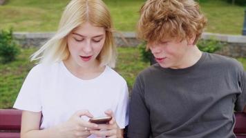 Teenage boy and girl hanging out at the park with a skateboard video