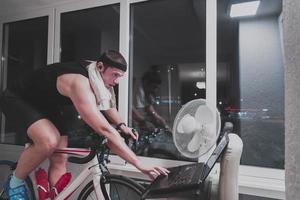 Man cycling on the machine trainer he is exercising in the home at night playing online bike racing game photo