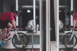 Man cycling on the machine trainer he is exercising in the home at night playing online bike racing game photo