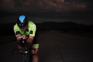 atleta de triatlón montando bicicleta rápido por la noche foto