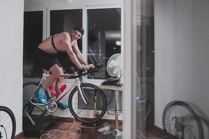 Man cycling on the machine trainer he is exercising in the home at night playing online bike racing game photo