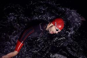 triathlon athlete swimming in dark night  wearing wetsuit photo